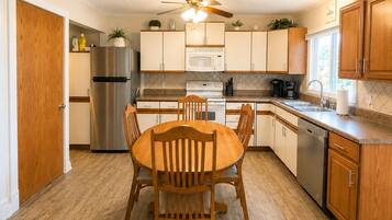 A compact kitchen with a dining table, wooden cabinets, a stainless steel refrigerator, and a ceiling fan.