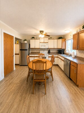 A compact kitchen with a dining table, wooden cabinets, a stainless steel refrigerator, and a ceiling fan. - Waterfront Escape on Crooked Lake - Kayaks & Boat Slip. Near Boyne Highlands! (Harbor Springs)