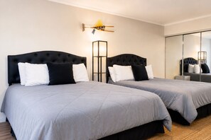 A hotel room with two beds, each with a tufted headboard, grey bedding, and a bedside table with a lamp. - Waterfront Escape on Crooked Lake - Kayaks & Boat Slip. Near Boyne Highlands! (Harbor Springs)