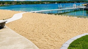 A beach with a concrete walkway, a wooden dock, and a clear blue sky.