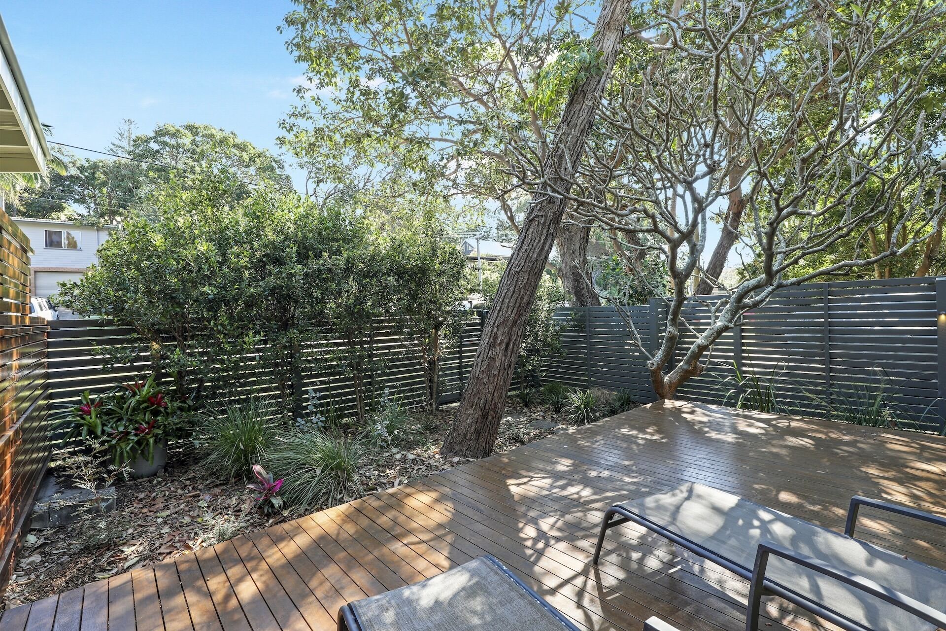 Una terraza de madera con barandilla de metal, rodeada por una valla negra y diversas plantas.
