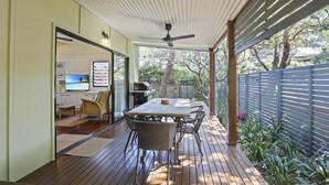 Un patio techado al aire libre con una mesa, sillas, un ventilador de techo y vista al jardín trasero.