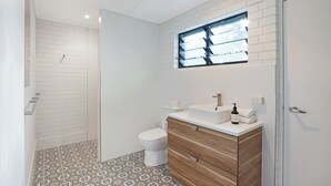 Un baño con ducha, inodoro y tocador con ventana sobre el lavabo.