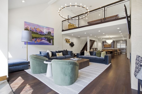 A spacious living area with a high ceiling, a staircase leading to an upper level, and a dining area in the background.