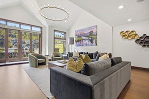 A modern living room with a grey sofa, a coffee table, and a painting of a mountain landscape.