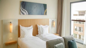 A hotel room with two beds, a sofa, a large window with a view of buildings, and a piece of abstract art on the wall. - Zephyr Agadir (Agadir)