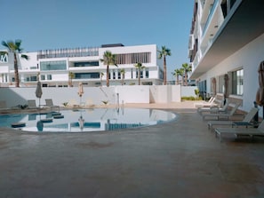 A modern hotel pool area with sun loungers and umbrellas, surrounded by palm trees and a multi-story building with large windows. - Zephyr Agadir (Agadir)