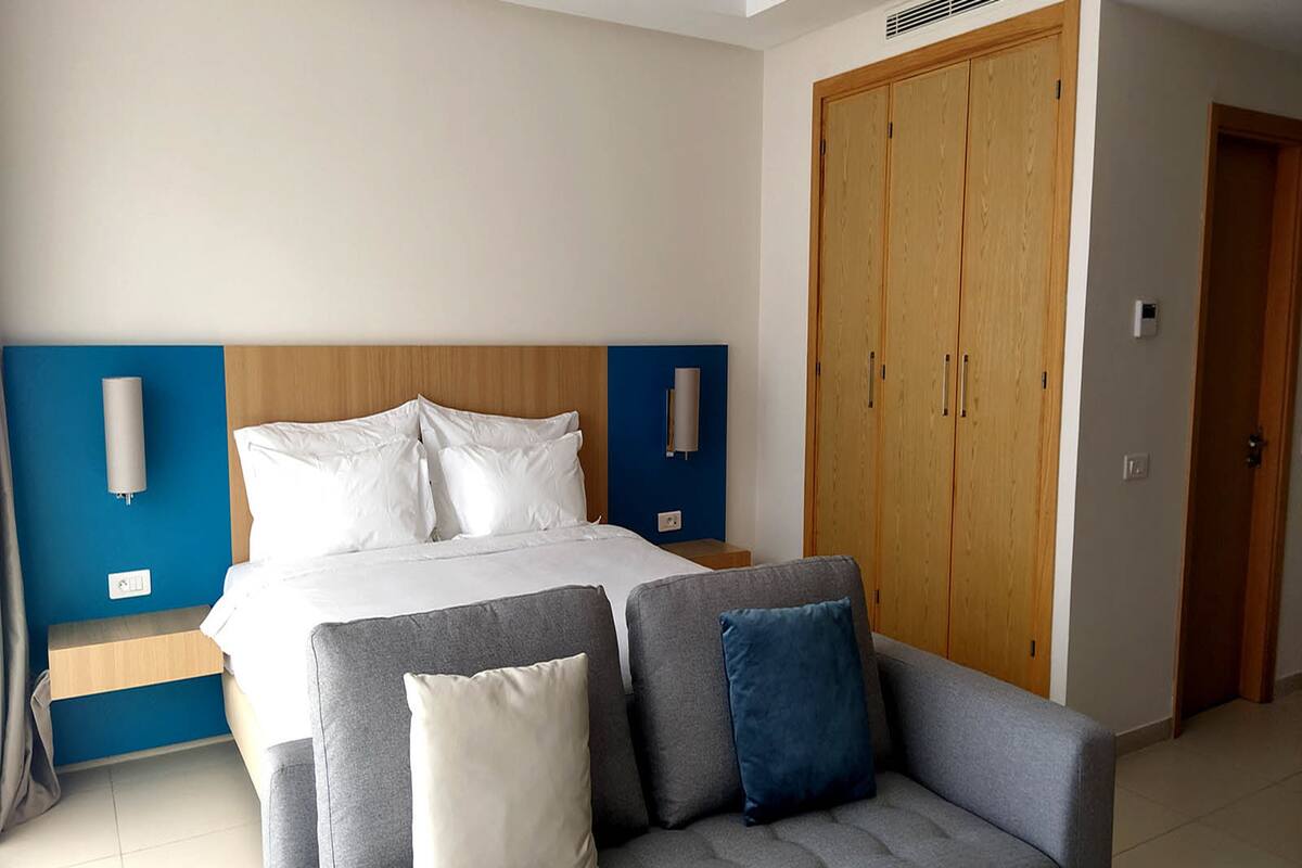 Ett hotellrum med en säng, en grå soffa med kuddar, en trägarderob och en blå accentvägg.