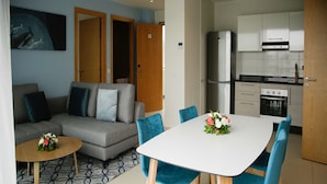A modern living space with a grey sofa, blue chairs, a white table, and a kitchen area with white cabinets and a stainless steel refrigerator. - Zephyr Agadir (Agadir)