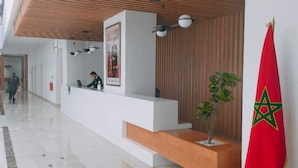 A modern reception area with a wooden ceiling, a reception desk, a potted plant, and a Moroccan flag. - Zephyr Agadir (Agadir)