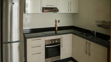 Una cocina compacta con refrigerador de acero inoxidable, horno integrado y encimera negra.
