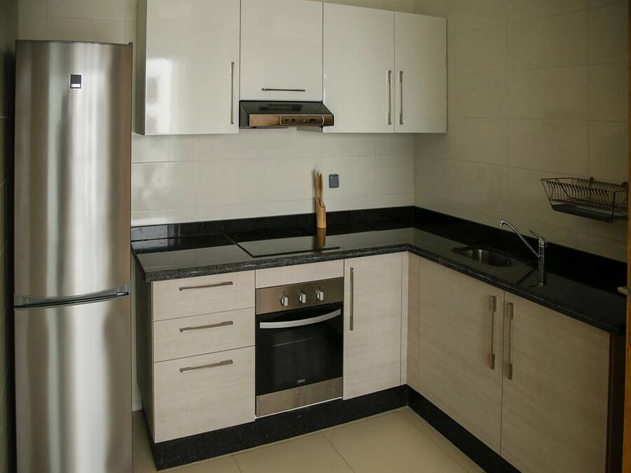 Una cocina compacta con refrigerador de acero inoxidable, horno integrado y encimera negra.