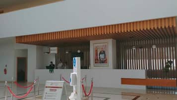 A modern lobby with a reception desk, a digital information kiosk, and a red rope barrier.