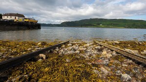 A coastal scene with a pier extending into the water, surrounded by rocks and seaweed. - 3 bedroom accommodation in Oban (Oban)