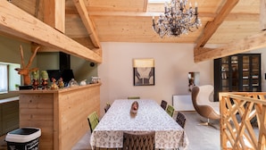 Ein Essbereich aus Holz mit einem für vier Personen gedeckten Tisch, umgeben von Stühlen. Eine Kristallleuchter hängt von der Decke, und im Hintergrund ist ein Schrank mit Glastüren zu sehen.