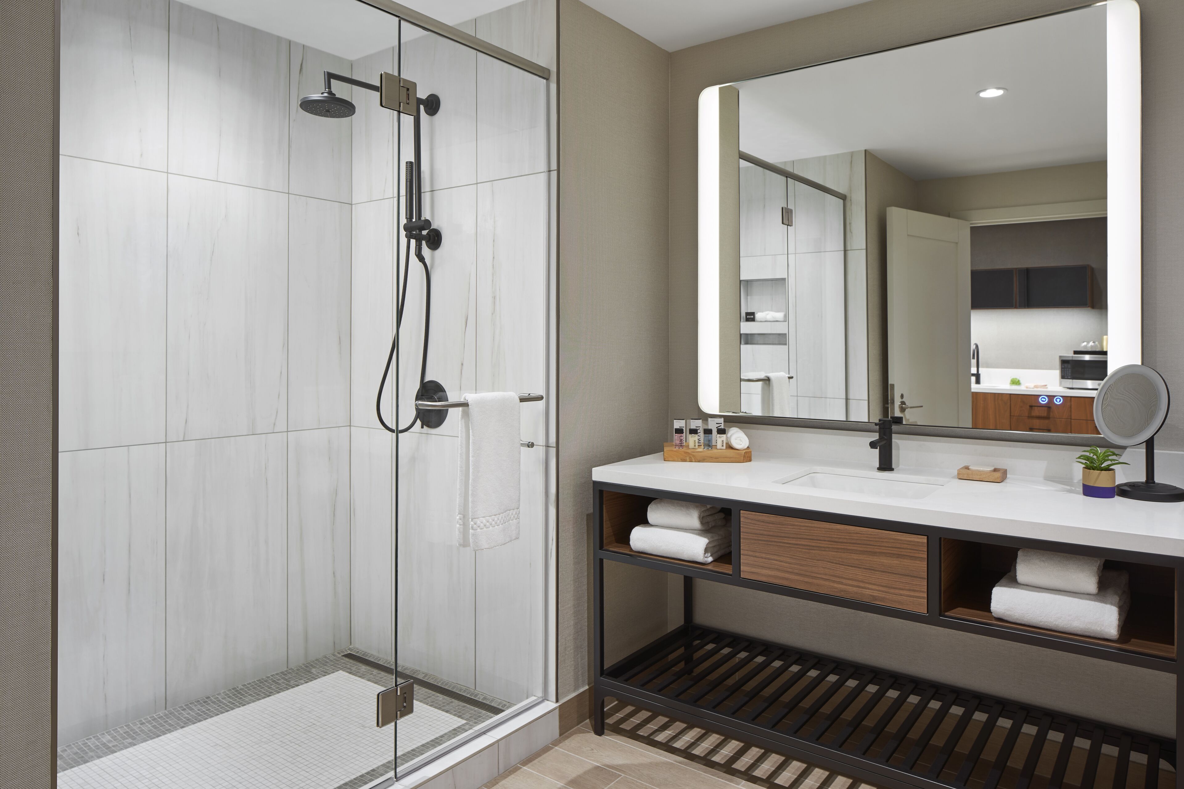 A modern bathroom with a glass-enclosed shower, a large mirror, and a vanity with shelves for towels and toiletries.