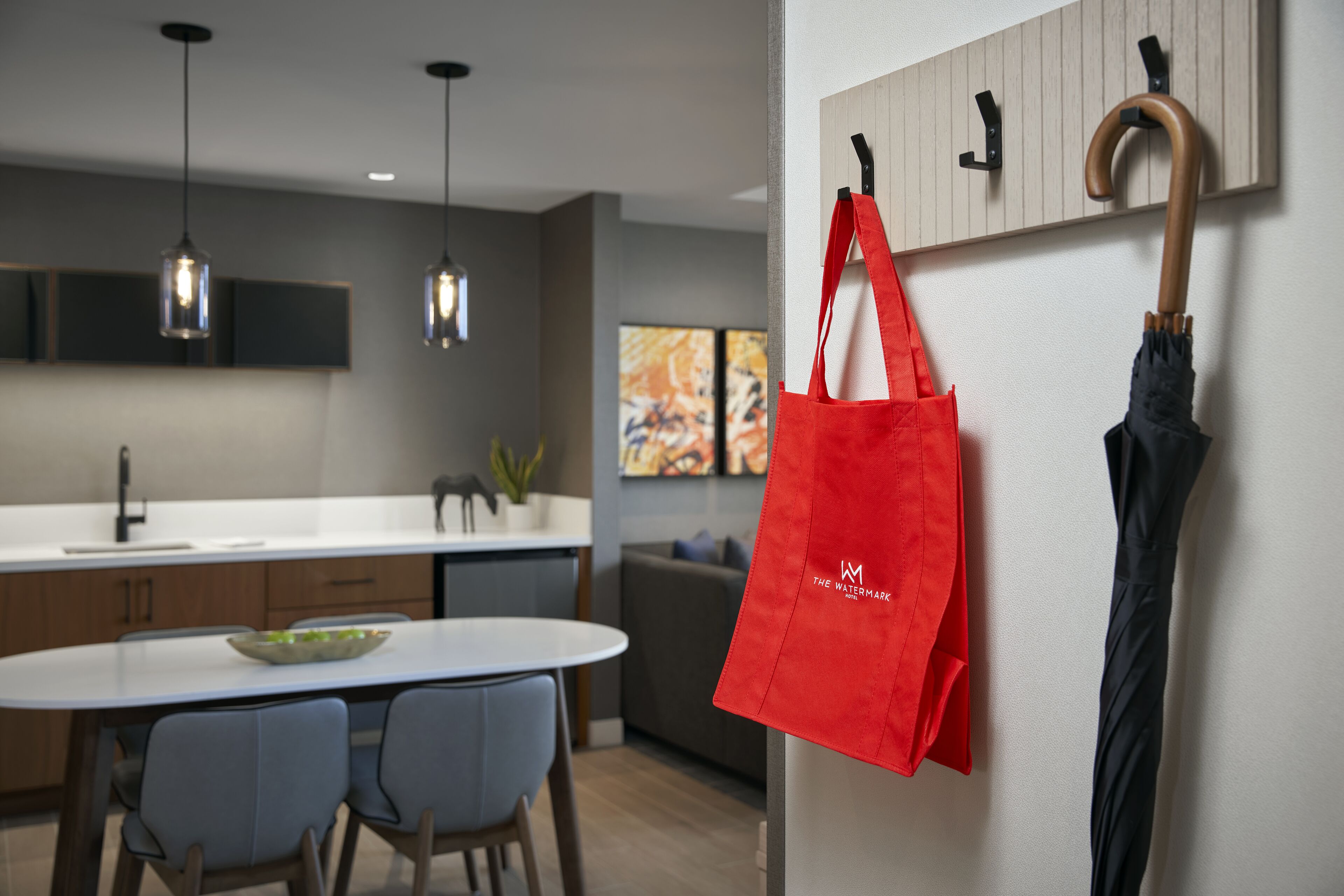 Una cocina moderna con iluminación colgante, un comedor con sillas y un bolso rojo colgado de un gancho.