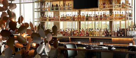 A bar with multiple shelves of bottles, a television screen, and a modern chandelier.