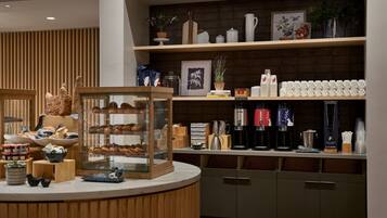Een bakkerijbalie met gebak, een koffiehoek en planken met decoratieve artikelen.