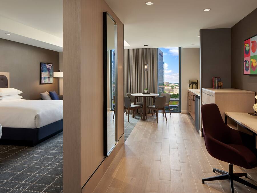 A hotel room with a bed, a desk, a chair, and a view of the city.