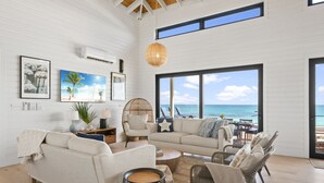 A spacious living room with a large window overlooking the sea, a white interior, and a cozy seating area. - BeauSoleil Beach House, Luxury Private Ocean Front with Infinity Pool/Hot Tub (Exuma)