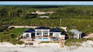 A beachfront property with a large house, a swimming pool, and a beach in the foreground. - BeauSoleil Beach House, Luxury Private Ocean Front with Infinity Pool/Hot Tub (Exuma)