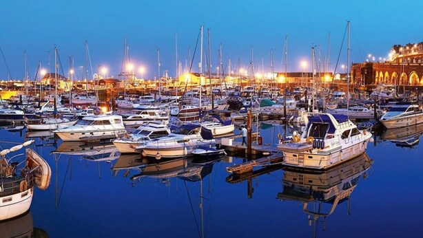 Un puerto deportivo con numerosos barcos amarrados de noche, iluminado por luces artificiales.