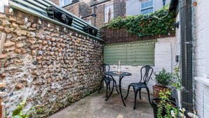 Un muro de piedra, una puerta verde y un pequeño patio con una mesa y sillas.