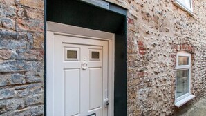 Una puerta blanca con aldaba, incrustada en un edificio de piedra con un letrero arriba que dice "Alma cottage".