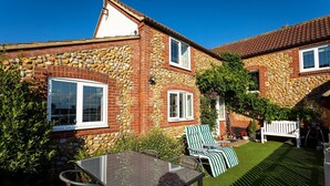 A stone house with a patio, outdoor seating, and a lawn. - Plum Guide - New Tricks (Norwich)