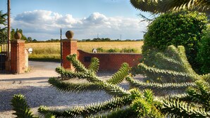 A gated entrance with brick walls and a gravel path leading to a field. - Plum Guide - New Tricks (Norwich)