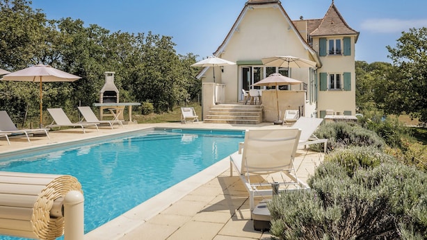 A pool area with lounge chairs, a barbecue grill, and a house with a tiled roof. - Mirandole, modern holiday home with views and heated pool (Martel)