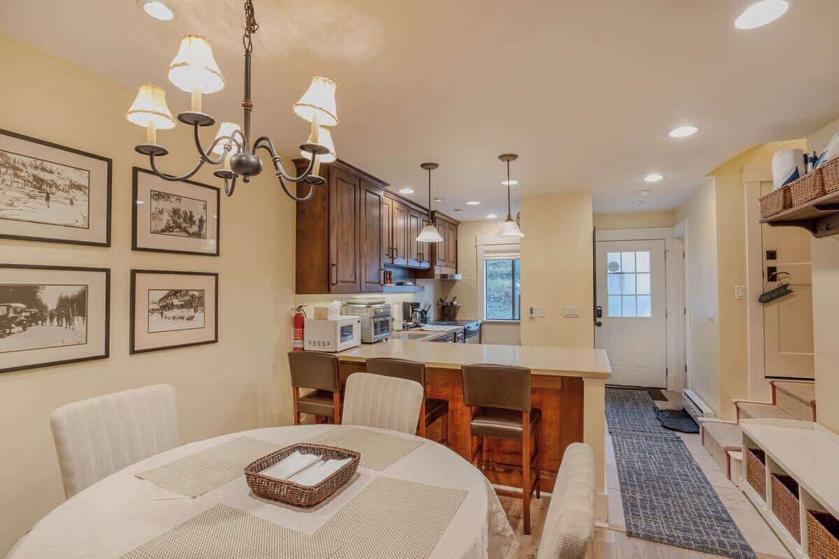 A modern kitchen with wooden cabinets, a dining area with a round table, and a chandelier.
