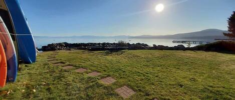 A grassy field with a clear sky, a body of water, and distant mountains.