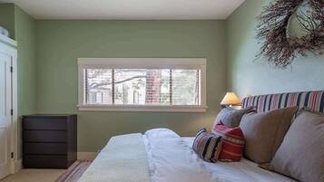 A bedroom with a bed, a window, a dresser, and a lamp.