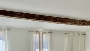 Ein modernes Wohnzimmer mit einer Couch, einem Esstisch mit Stühlen und einem großen Fenster mit durchsichtigen Vorhängen.
