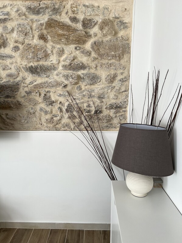 A room with a stone wall, a white floor, and a lamp with a white base and dark shade.