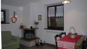 A cozy living room with a fireplace, a dining table with a red tablecloth, a green armchair, and a hanging light fixture. - Sunflowers - Pink apartment  (Camerino)