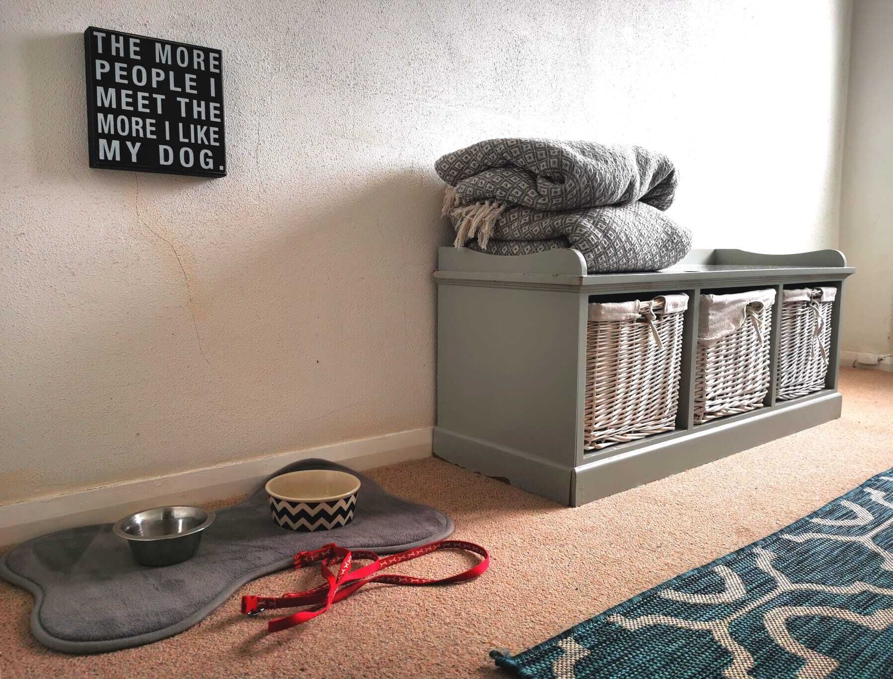 Quarto que aceita animais de estimação, com cama para cachorro, comedouro, guia e placa na parede.