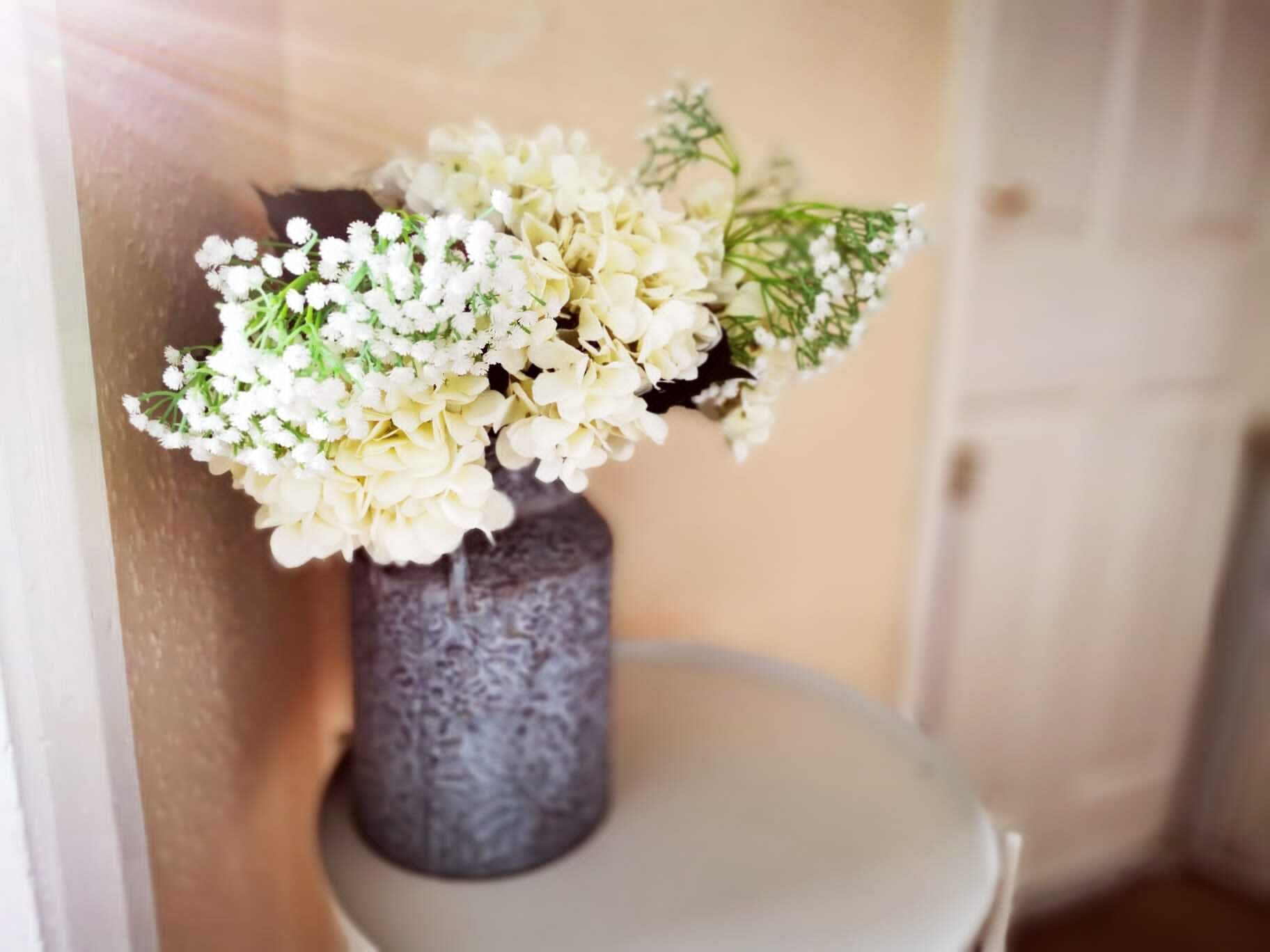 A vase with white flowers and green foliage on a table.