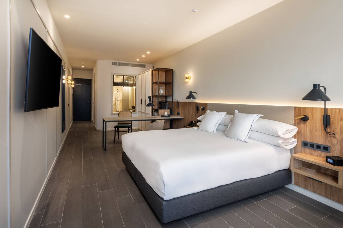 A modern hotel room with a large bed, a desk, and a TV mounted on the wall.