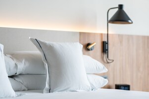 A neatly made bed with white linens and pillows, a modern wall-mounted lamp, and a wooden panel wall.
