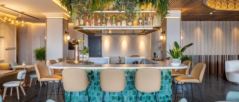 Zona de bar moderna con una isla central, taburetes y un techo decorativo con plantas colgantes.
