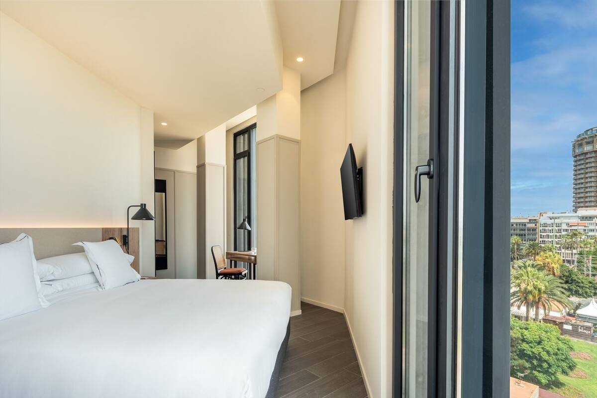 A modern hotel room with a large bed, a desk, and a TV mounted on the wall.