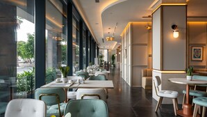 A modern restaurant with long tables and chairs, large windows, and indoor plants.