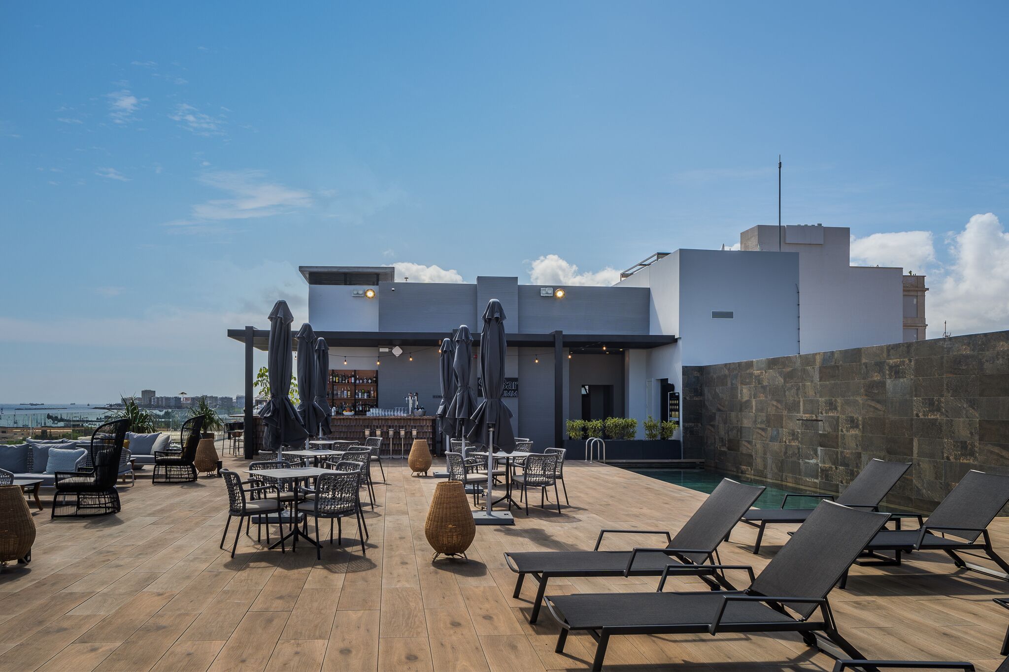 A rooftop bar with outdoor seating, a pool, and a view of the city skyline.