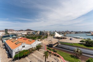 Un paisaje urbano costero con un edificio blanco destacado de techo rojo, un puerto deportivo y un cielo despejado.