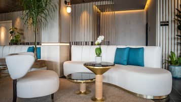 Een moderne woonkamer met een witte bank, een ronde salontafel en een stoel. Er staat een kamerplant en er hangt een wandlamp.