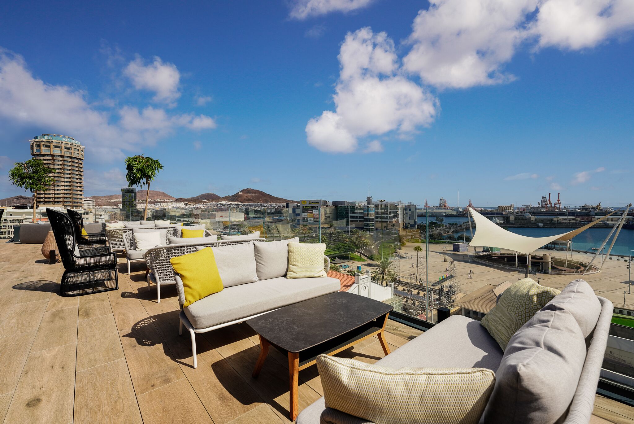 A rooftop terrace with outdoor furniture, a view of the city, and a body of water in the background.