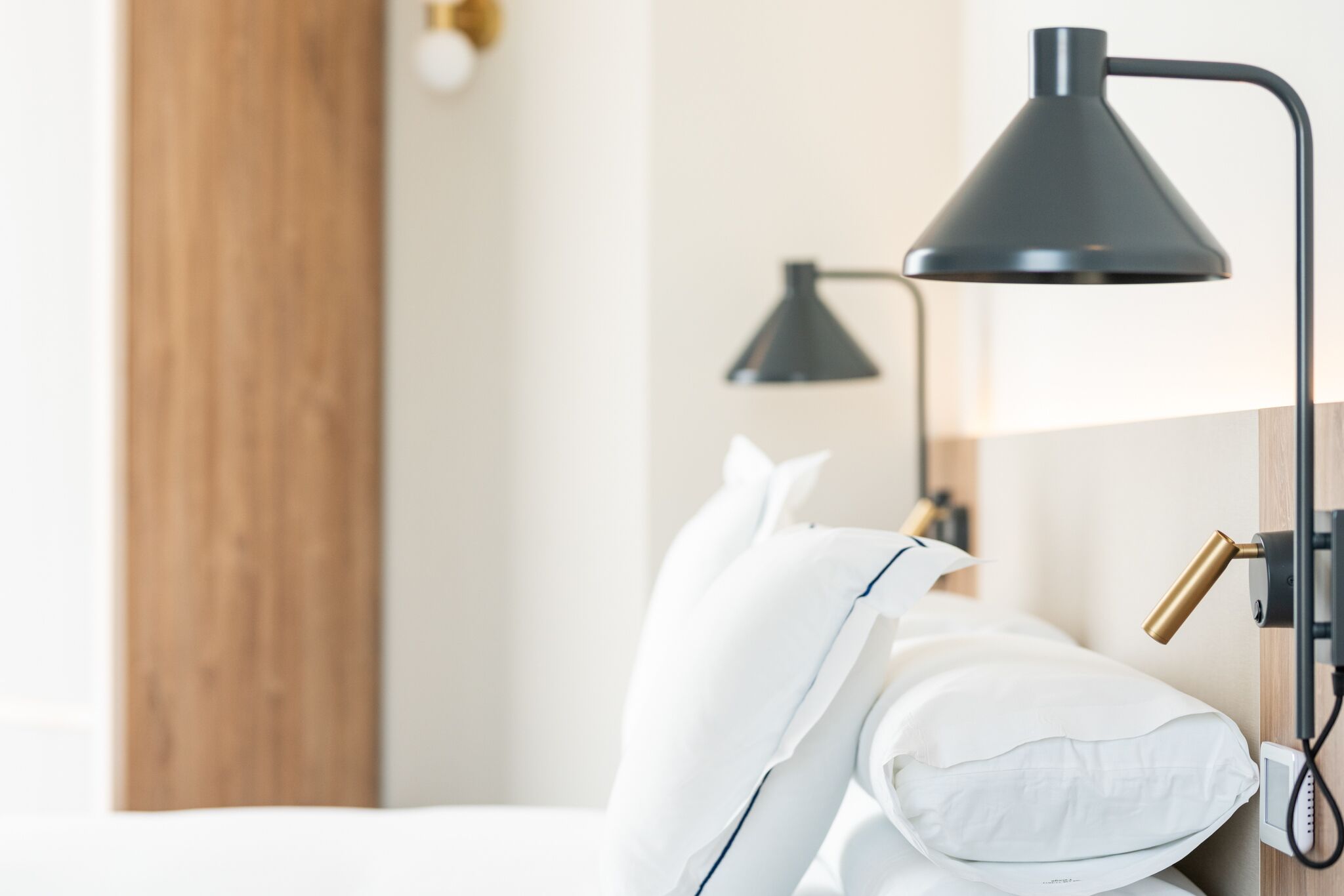 Une chambre d’hôtel bien rangée, avec un lit, des oreillers blancs et une lampe de bureau noire.
